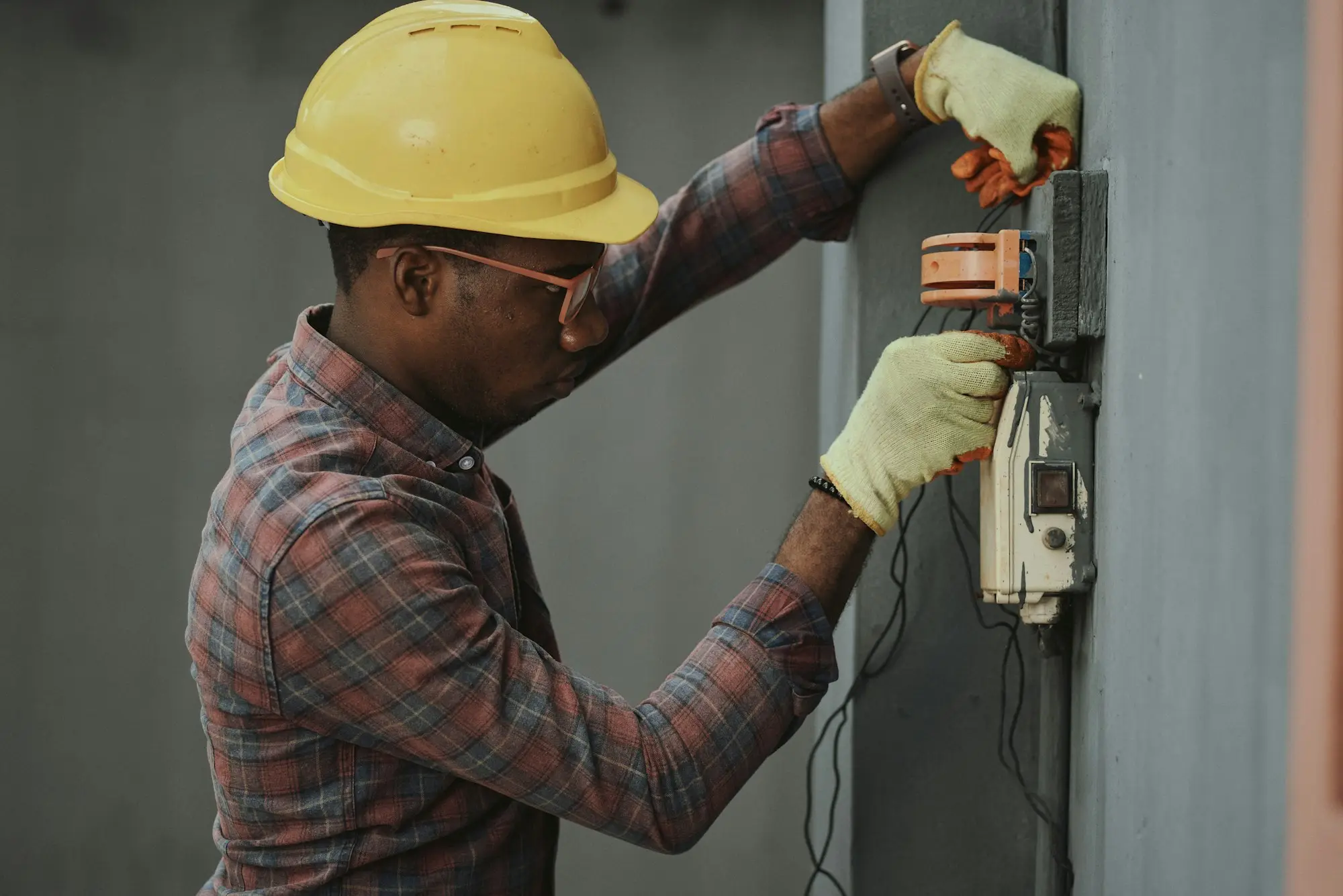 Tradesperson in a plaid shirt and yellow hard hat holding tools on site