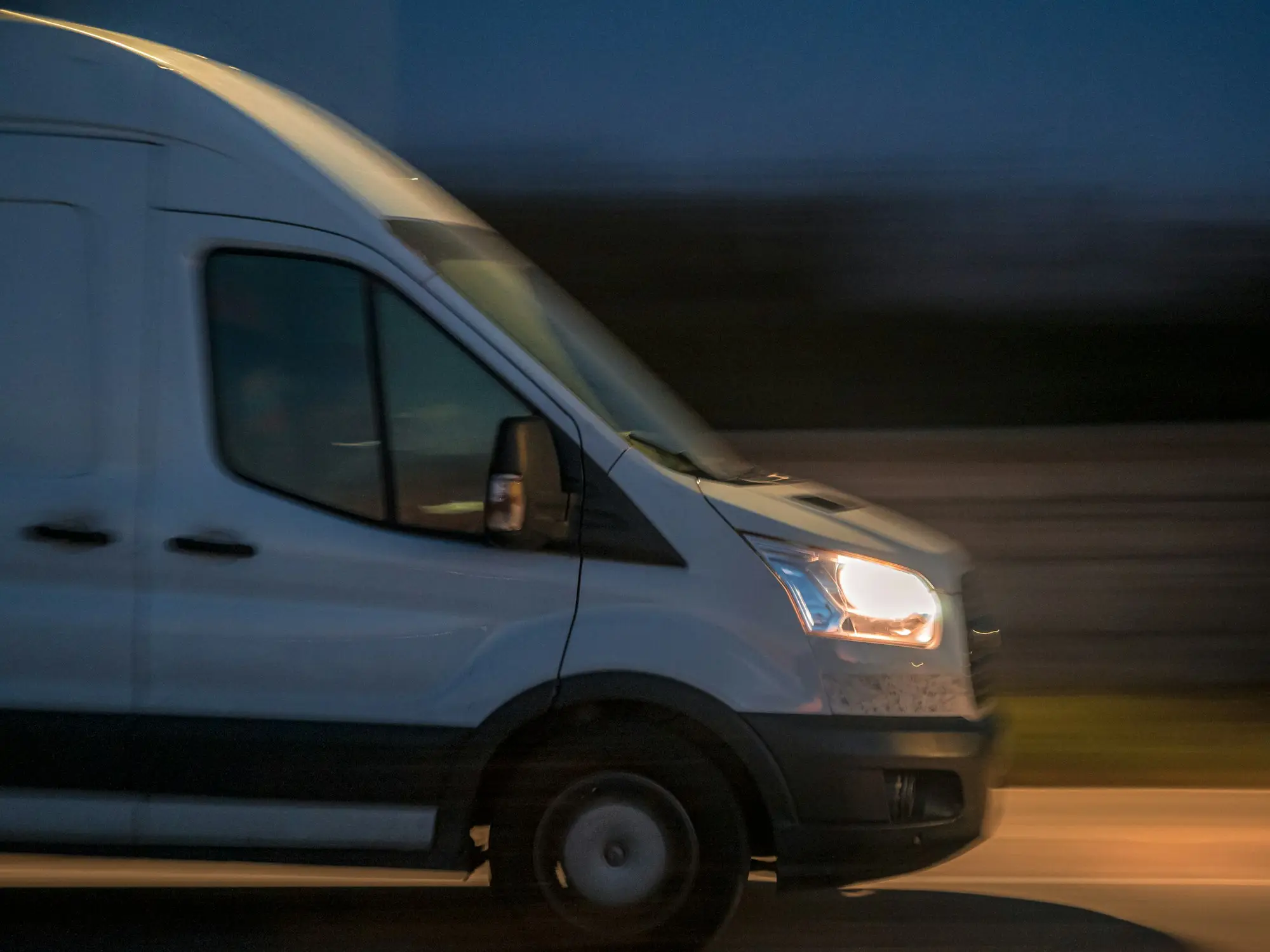 White work van driving down a city street at night