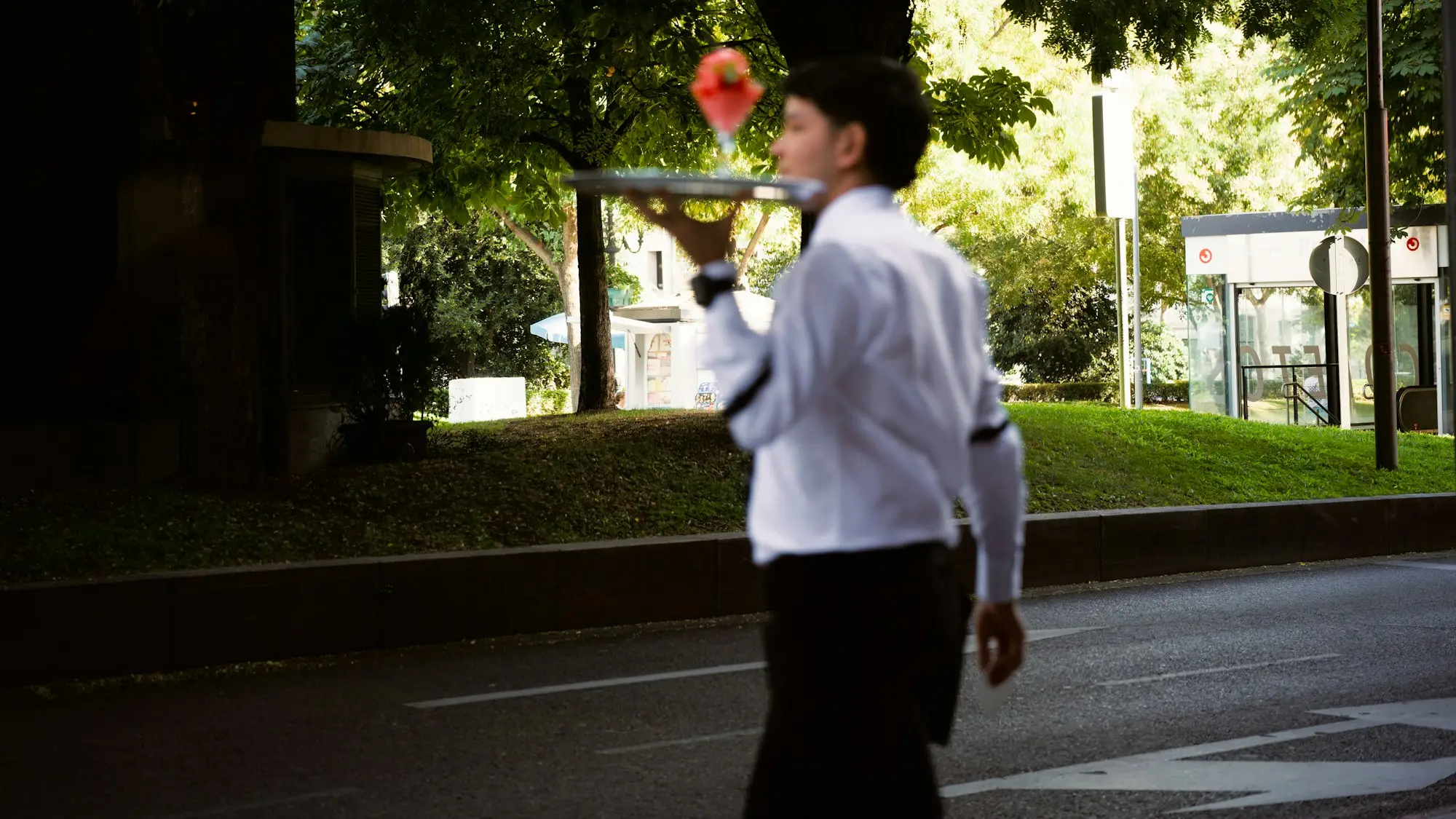 Waiter in a white shirt carrying a tray of drinks to an outdoor table